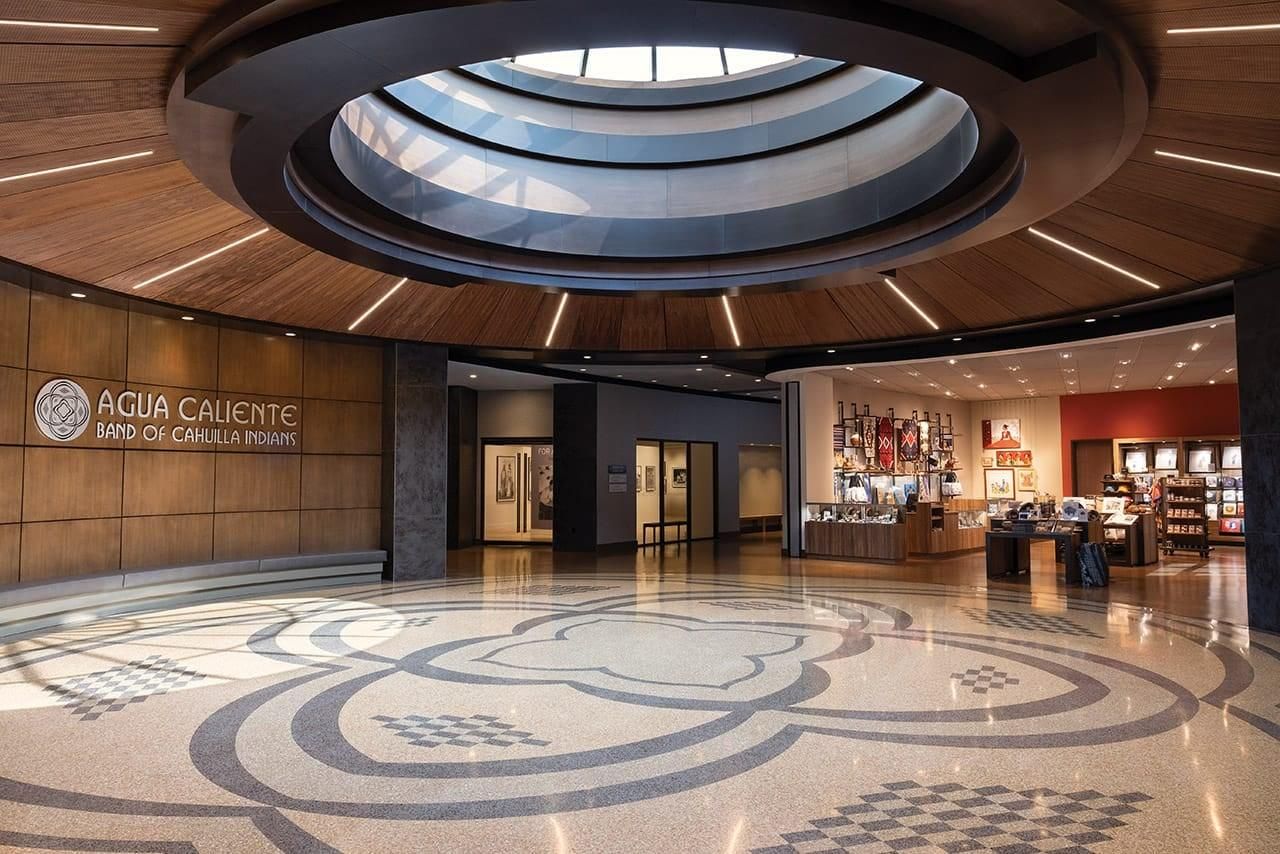 A round lobby with a circular skylight set in a wood ceiling, a patterned terrazzo floor, and the words Agua Caliente Band of Cahuilla Indians on a wood wall.